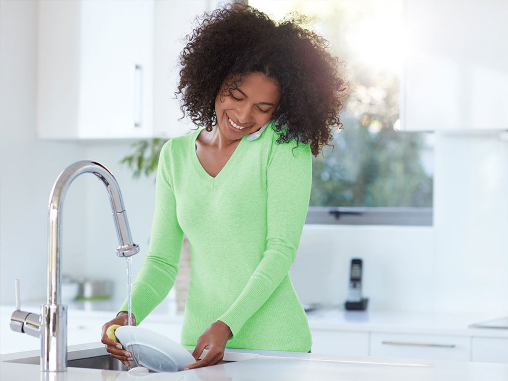 Smiling woman cleaning plate at kitchen sink
