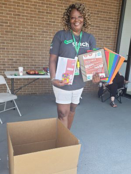 A Cinch employee, holding folders, crayons and other school supplies, volunteers at the Back to School Drive